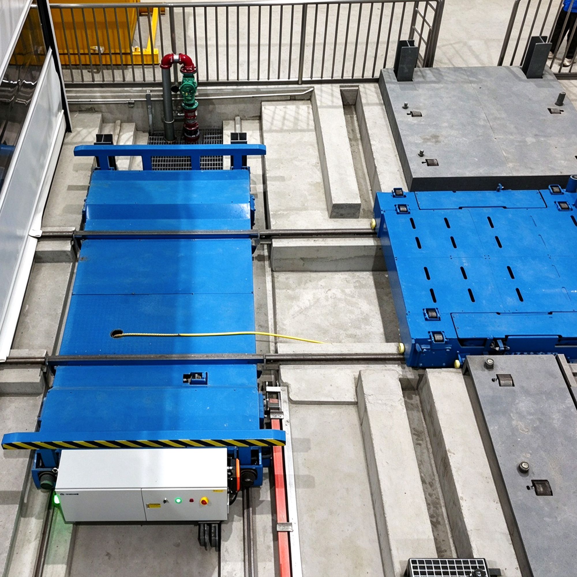Overhead view of blue mother and daughter transfer trolleys on rails between concrete bays